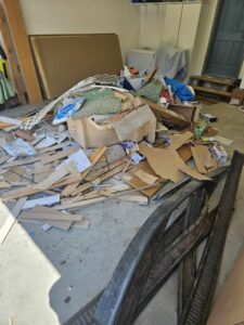 A large pile of mixed debris, including wood, cardboard, and carpet, on a garage floor for cleanout by Primetime Hauling and Junk Removal in Spokane, WA.
