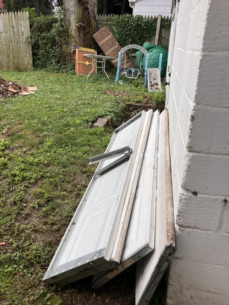Old garage door panels leaning against a building, ready for junk removal by HaulPros in Erie, PA.