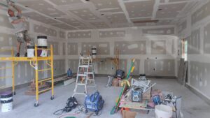 A worker finishing drywall in a large garage or open space, showcasing expert work by NED CO. in Springfield, MA.
