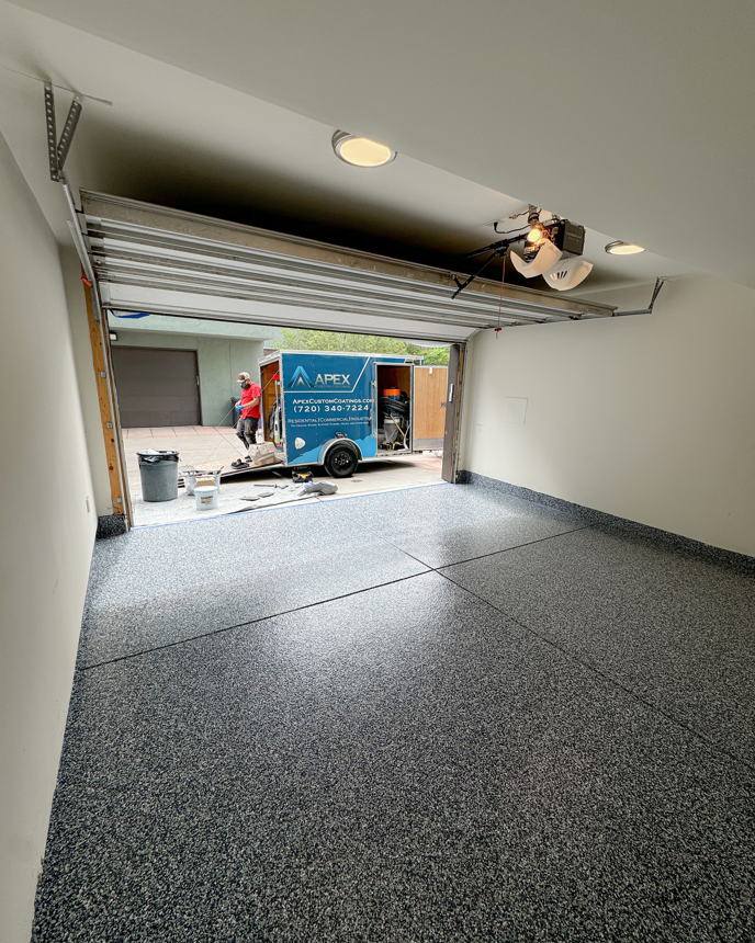 A completed garage floor coating project with a worker and Apex Custom Coatings trailer in Middleton, WI