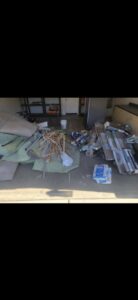 A garage floor covered with construction debris, old carpet, wood scraps, and various junk items for removal by The Junkporter Junk Removal in Las Vegas, NV.