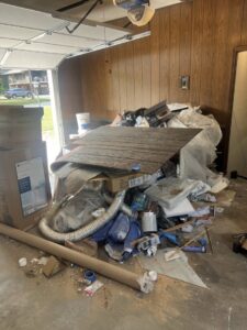 A garage filled with a large pile of debris and junk, illustrating a thorough cleanout service by Little Tykes Property Preservation in Independence, MO.