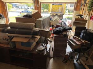 A garage filled with old furniture, rolled carpets, and junk, with a Got Rubbish truck visible outside in Jersey City, NJ