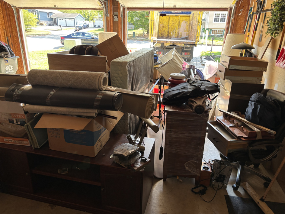 A garage filled with old furniture, rolled carpets, and junk, with a Got Rubbish truck visible outside in Jersey City, NJ
