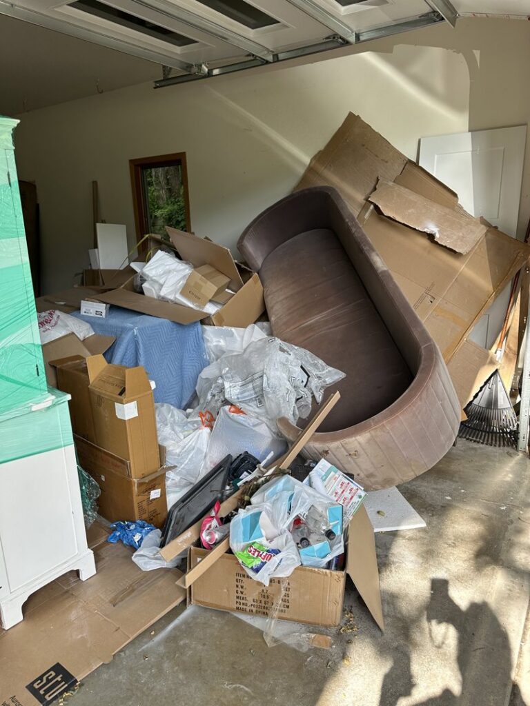 A garage completely full of junk, including a large couch and cardboard boxes, awaiting removal by KJ Haul Away Junk Removal in Cedar Rapids, IA.