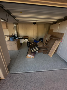 A garage cluttered with cardboard boxes, wood, and other junk, awaiting removal by Tough Guy Junk Removal in Fountain Hills, AZ.