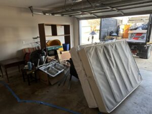A cluttered garage filled with household junk and a Strong Lion Junk Removal truck ready to haul it away in Fayetteville, AR.