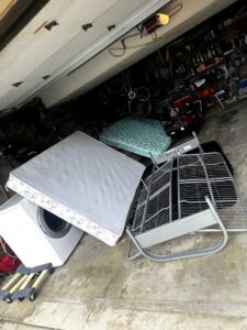 A garage filled with a mattress, washing machine, bed frame, and other large items, indicating a junk removal service by Junk-O-Haulics in Westmoreland, TN.