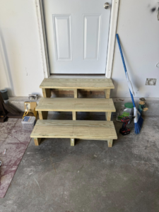 Three newly installed wooden steps leading to a door inside a garage, built by Daniels Handyman Services in Warwick, RI.