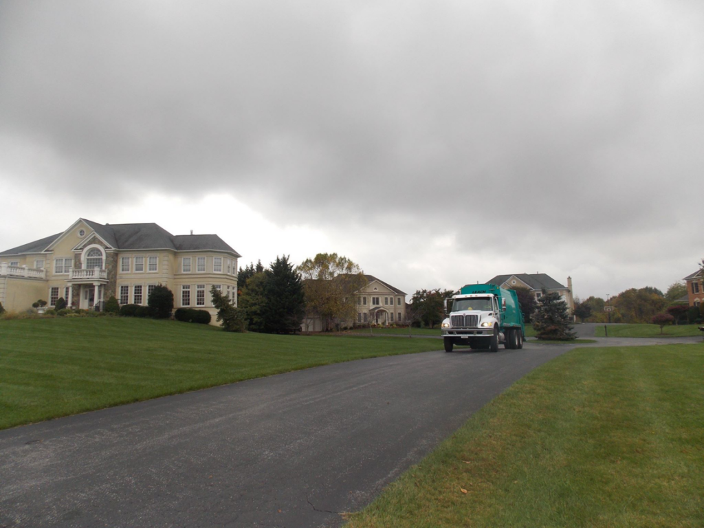 An Elegant Recycling & Refuse Services Inc. garbage truck collecting waste on a residential street in Spencerville, MD.