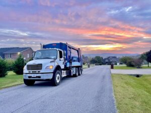 A J.E. McMurtry Disposal & Recycling garbage truck driving on a residential street at sunrise in Nashville, TN.