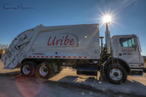 A Uribe Refuse Services garbage truck parked under a bright sun in Lincoln, NE.