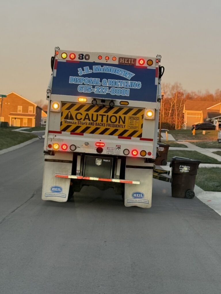 The back of a J.E. McMurtry Disposal & Recycling garbage truck with a brown trash bin ready for pickup in Nashville, TN.