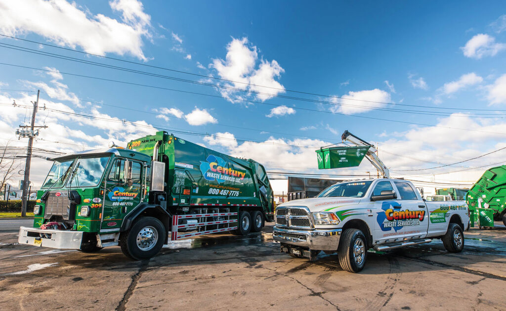 A Century Waste Management garbage truck and a pickup truck lifting a dumpster for junk removal in Sterling Heights, MI.