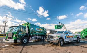 A Century Waste Management garbage truck and a pickup truck lifting a dumpster for junk removal in Sterling Heights, MI.