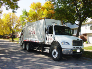 A Uribe Refuse Services garbage truck parked on a residential street with autumn trees in Lincoln, NE.