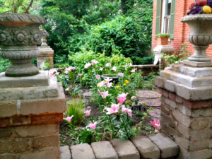 A garden entrance featuring brick pillars and stepping stones with blooming flowers by Massa Paving Company in Cincinnati, OH.