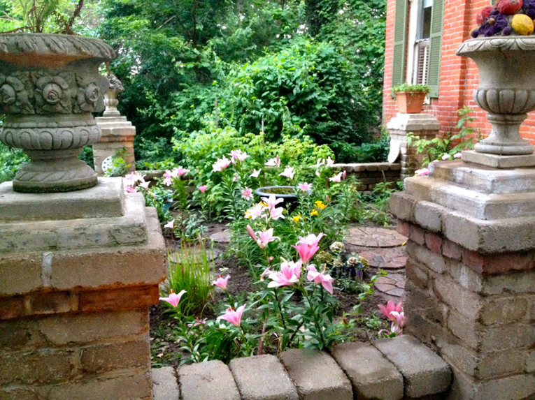 A garden entrance featuring brick pillars and stepping stones with blooming flowers by Massa Paving Company in Cincinnati, OH.