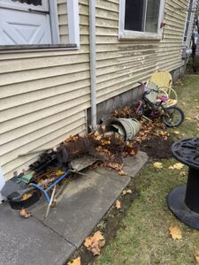 A pile of old garden tools, leaves, and a child's bicycle next to a house, ready for removal by Junk Removal Brothers in Worcester, MA.
