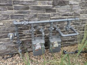 Gas meter and piping installation on a stone wall by Top-Notch Plumbing, Heating & Air in Greeley, CO.