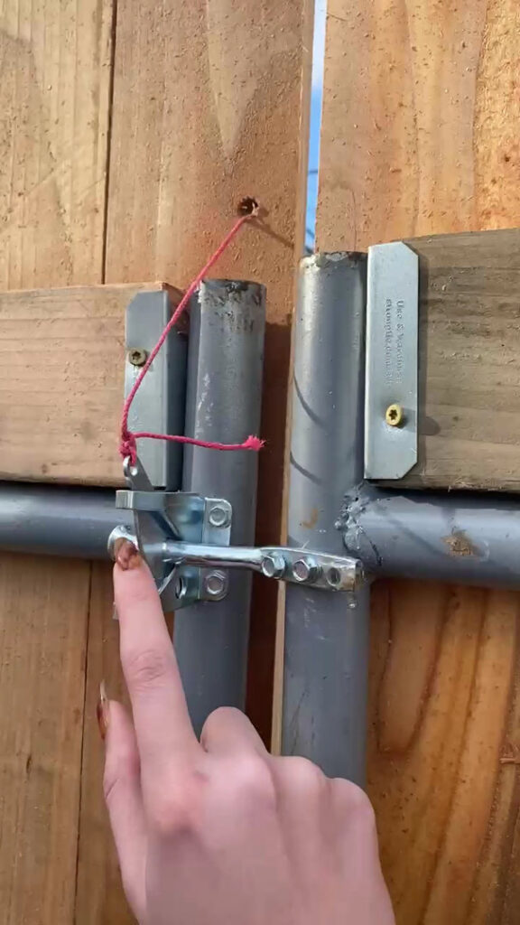 A hand demonstrating the operation of a newly installed metal gate latch on a wooden fence gate by J & M Fence Co. in Vancouver, WA.