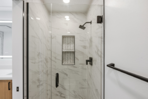 A modern glass shower enclosure with black fixtures and tiled walls by BelRed Construction in Bellevue, WA.