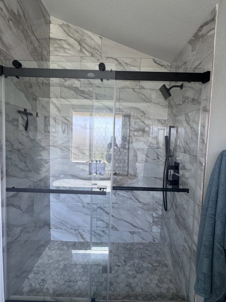 A modern glass shower with marble-look wall tiles and hexagonal floor tiles by A&R Home Improvements in El Paso, TX