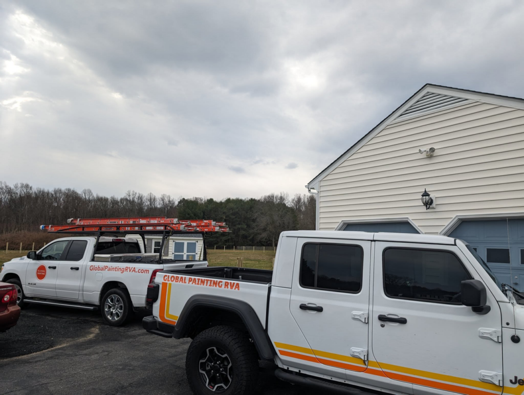 Two Global Painting RVA work trucks with ladders parked outside a house in Richmond, VA, ready for a painting job.