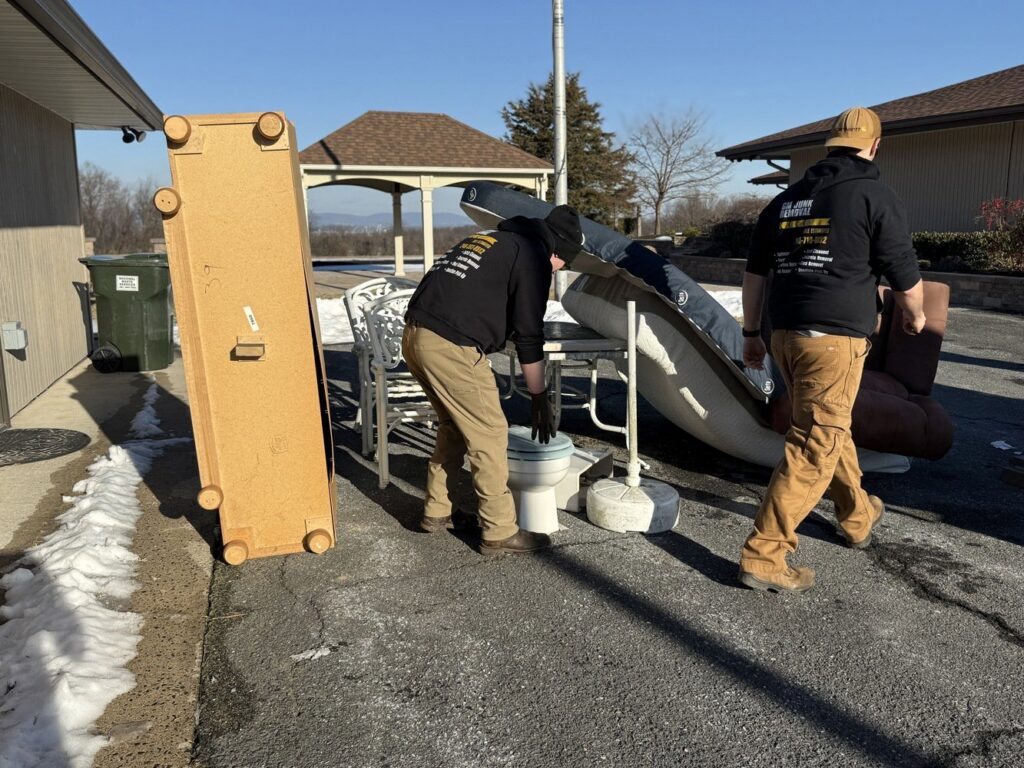 GM Junk Removal team members actively moving large furniture and a toilet during a cleanup job in Frederick, MD.