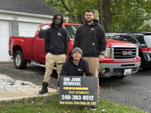 The GM Junk Removal team posing with their service sign in front of a red pickup truck in Frederick, MD.