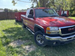 A GMC pickup truck towing a red dump trailer from The Dump Town for junk removal in Detroit, MI.