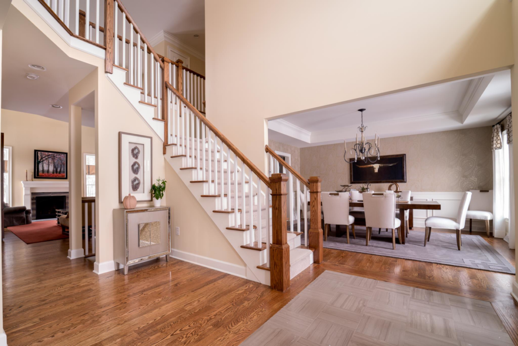 A grand entryway with a wooden staircase and hardwood floors, leading to a dining room, by Charlew Builders in Schenectady, NY.