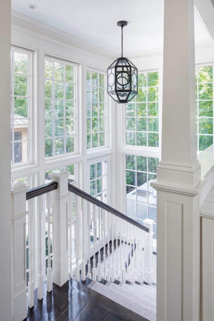 A grand entryway featuring a multi-story staircase, large windows, and a modern light fixture by FH Perry Builder in Hopkinton, MA.