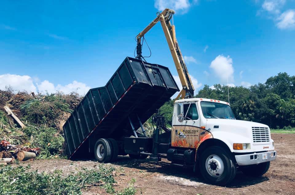 A grapple truck loading tree debris into a dumpster during a cleanup by Blaze Tree Service Inc in Orlando, FL
