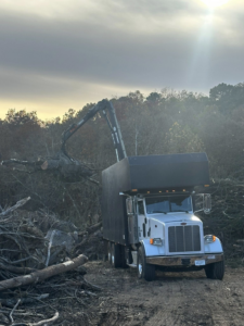 A grapple truck loads a large pile of tree logs and branches for removal by 4M Tree Service in Knoxville, TN.