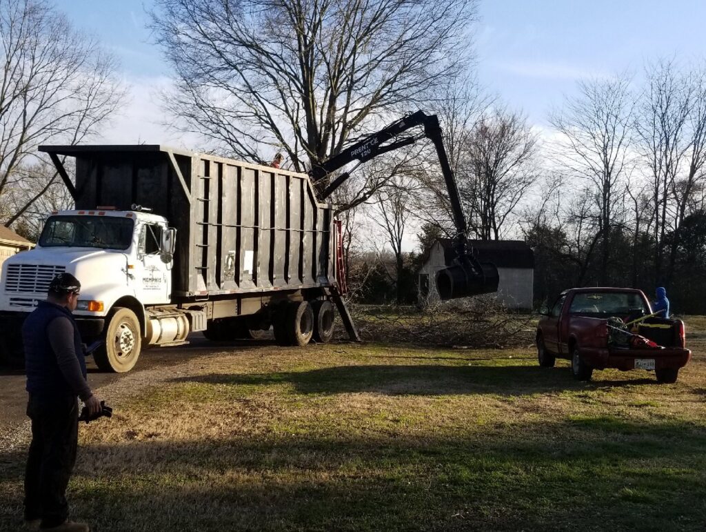 A grapple truck efficiently loading tree branches into a large dump truck for cleanup by All Star Tree Service in Memphis, TN.