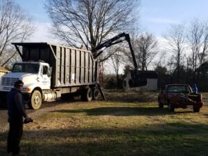 A grapple truck efficiently loading tree branches into a large dump truck for cleanup by All Star Tree Service in Memphis, TN.