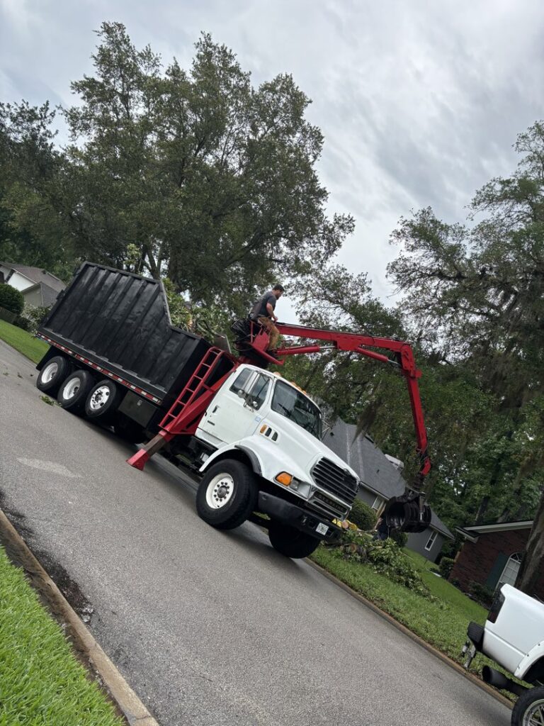 A grapple truck removing tree debris from the roadside, demonstrating cleanup services by Souza & Son's Tree Service in Jacksonville, FL.