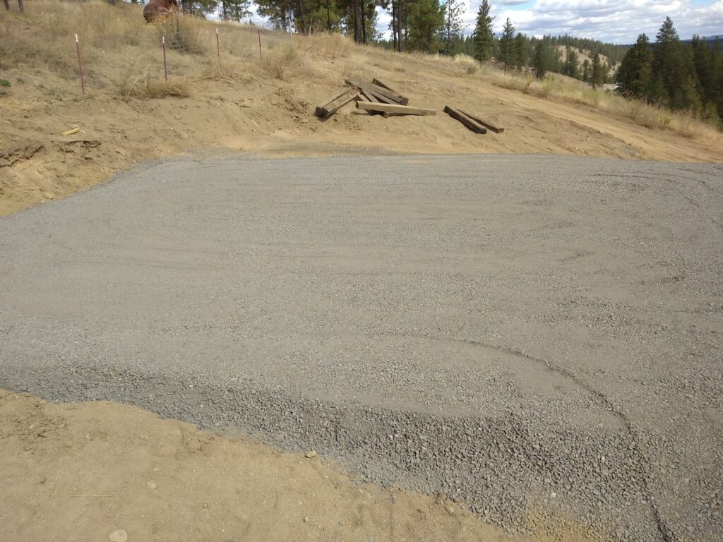 A newly leveled and graveled area, likely for a driveway or pad, prepared by Aspen Excavation in Spokane, WA.