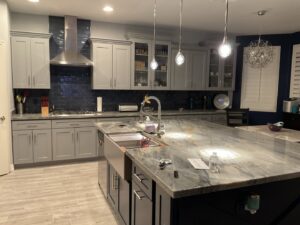 A modern kitchen remodel with gray cabinets, dark subway tile backsplash, and a large island with a farmhouse sink by LJ Builders in Chandler, AZ