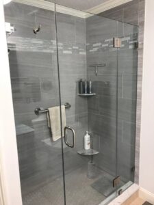 A modern gray tiled shower with a glass door and built-in shelves by Prenga Remodeling in Orange, CT