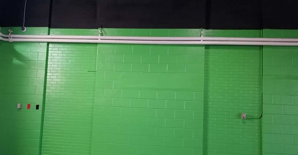 A freshly painted green brick wall with white pipes and electrical outlets, showcasing handyman work by Reshaud Renovation LLC in Richmond, VA.