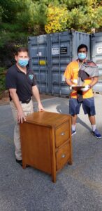 Green Clover team members preparing to remove a wooden filing cabinet near shipping containers in Quincy, MA.