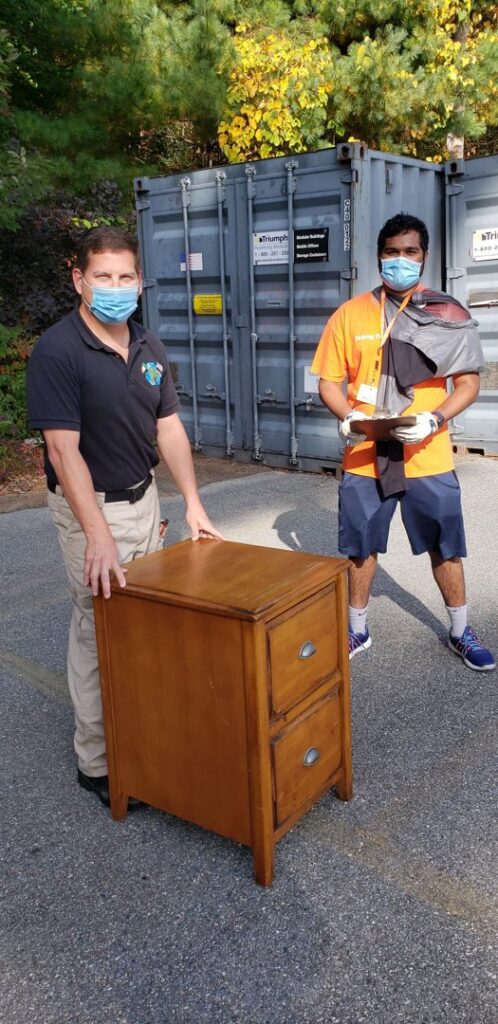 Green Clover team members preparing to remove a wooden filing cabinet near shipping containers in Quincy, MA.
