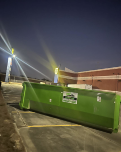 A green dumpster from Top Line Dumpsters LLC placed at a Best Buy parking lot at night in Hammond, LA.