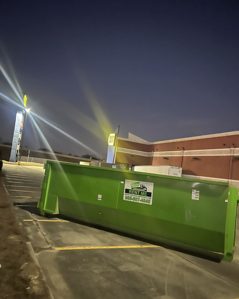 A green dumpster from Top Line Dumpsters LLC placed at a Best Buy parking lot at night in Hammond, LA.