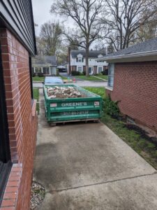 A green dumpster filled with construction debris in a residential driveway from Greene's Roll Off Service in Indianapolis, IN.