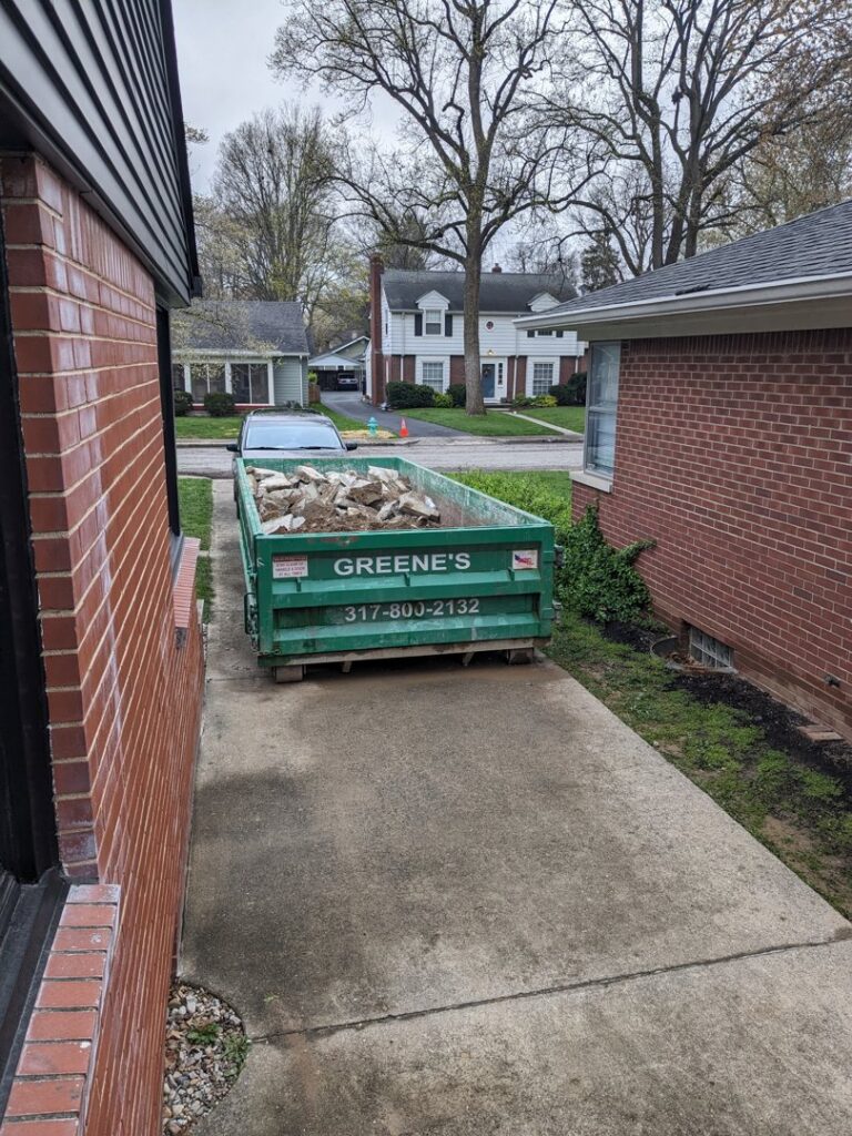 A green dumpster filled with construction debris in a residential driveway from Greene's Roll Off Service in Indianapolis, IN.
