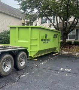 A bright green dumpster being delivered to a parking lot by Wood Property Services & Dumpster Rental LLC in Wilmington, NC.