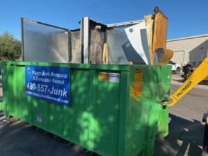 A large green Happy Junk Removal dumpster filled with various items of junk, ready for transport in Mesa, AZ.